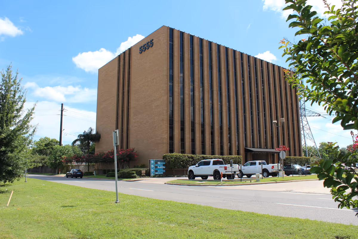 Tall brick building with vertical windows, a parking lot, and blue sky.