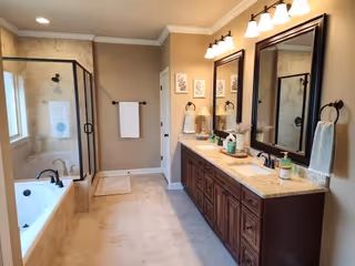 Bright bathroom featuring double-sink vanity, mirrors, glass shower, and bathtub.