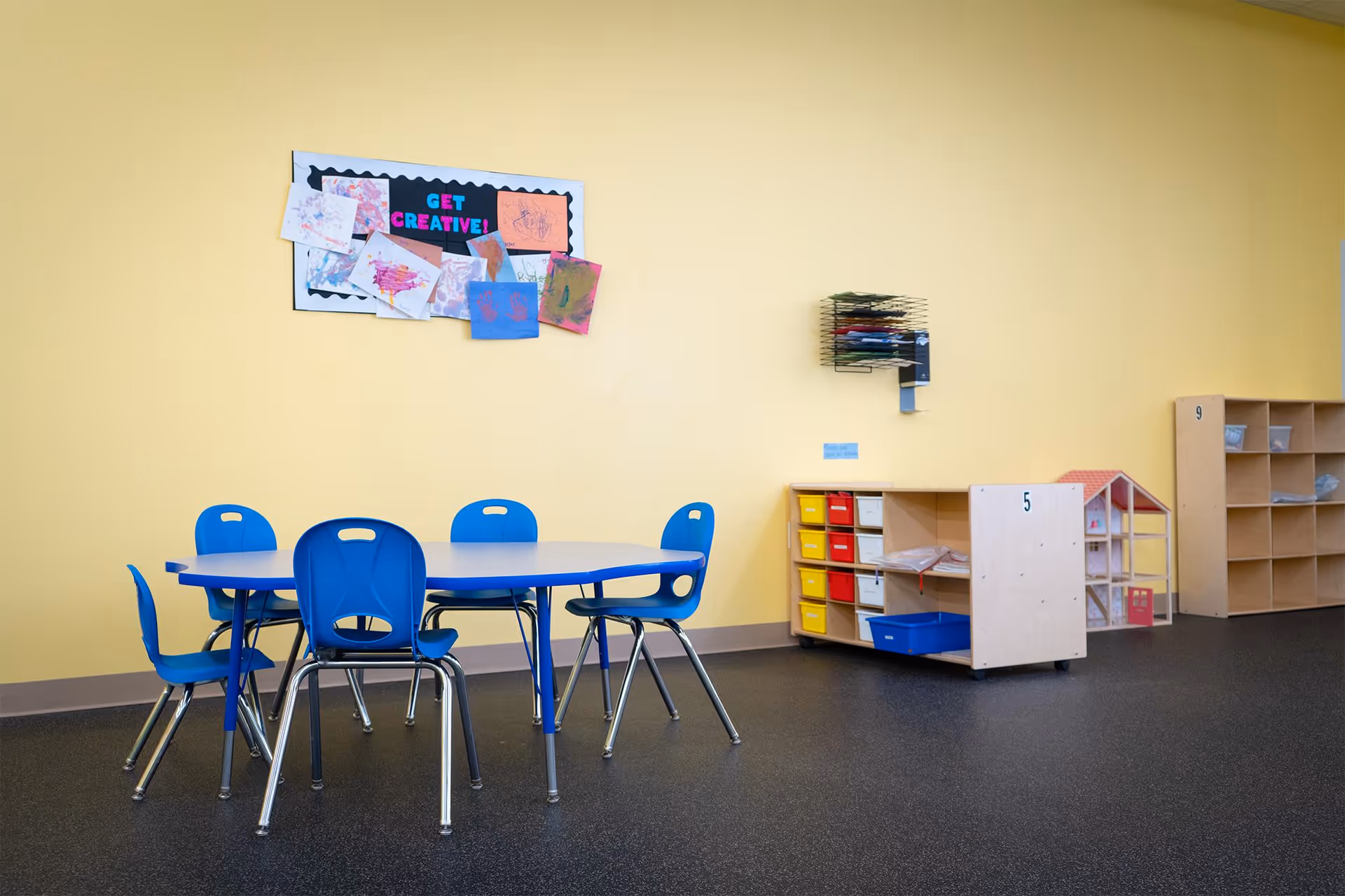 Yellow-walled therapy room with blue tables, chairs, and wooden storage cubbies.