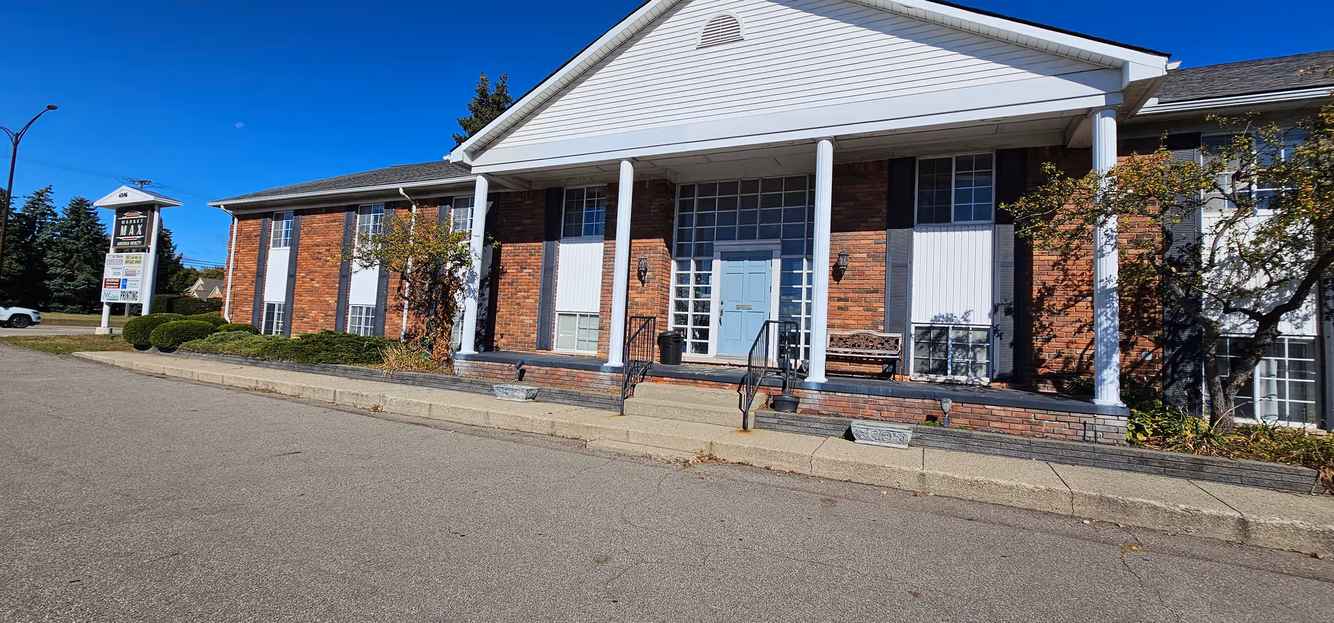 Exterior view of a brick senior living facility with a blue front door, columns, and steps.