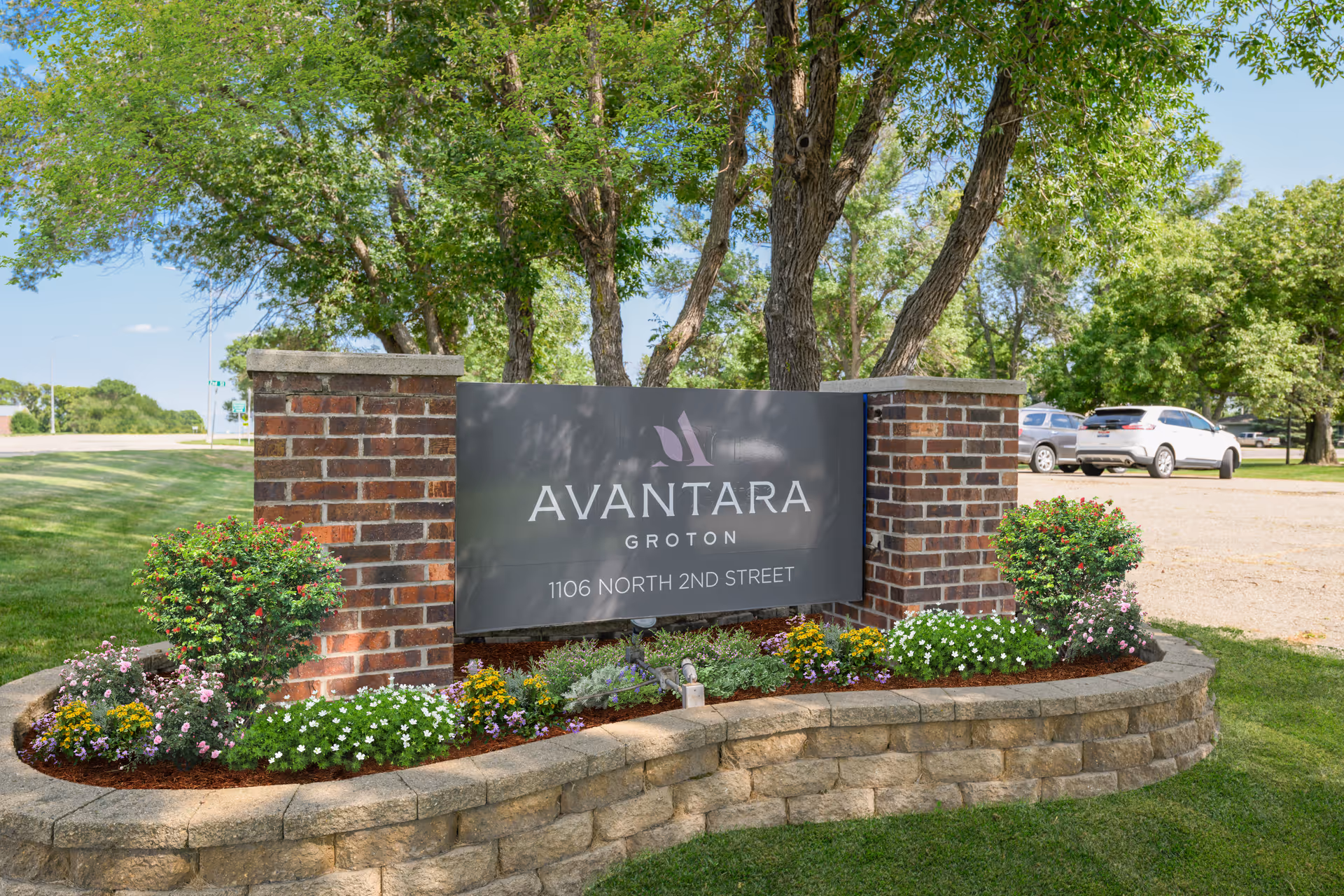 Brick sign for Avantara Groton surrounded by flower beds and trees in a landscaped yard.