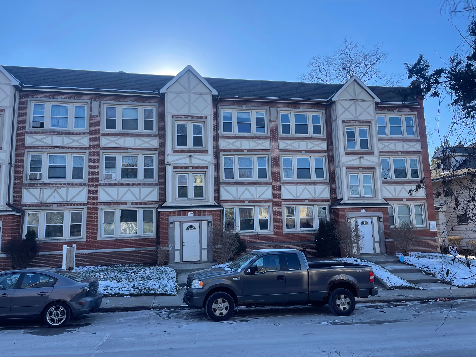 Three-story brick building with beige Tudor-style accents and parked cars along a snowy street.