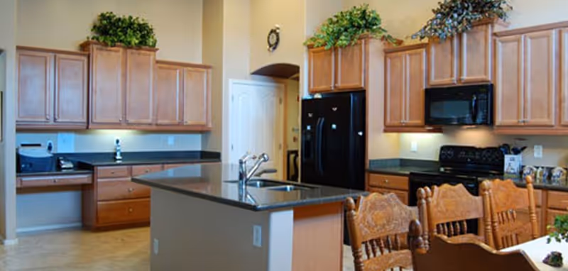 Modern senior living kitchen with island, wooden cabinets, and dining area.