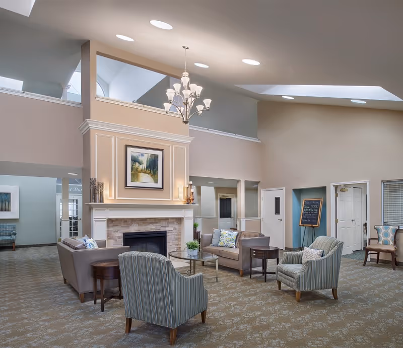 Spacious lounge in a senior living facility with sofas, fireplace, and chandelier.