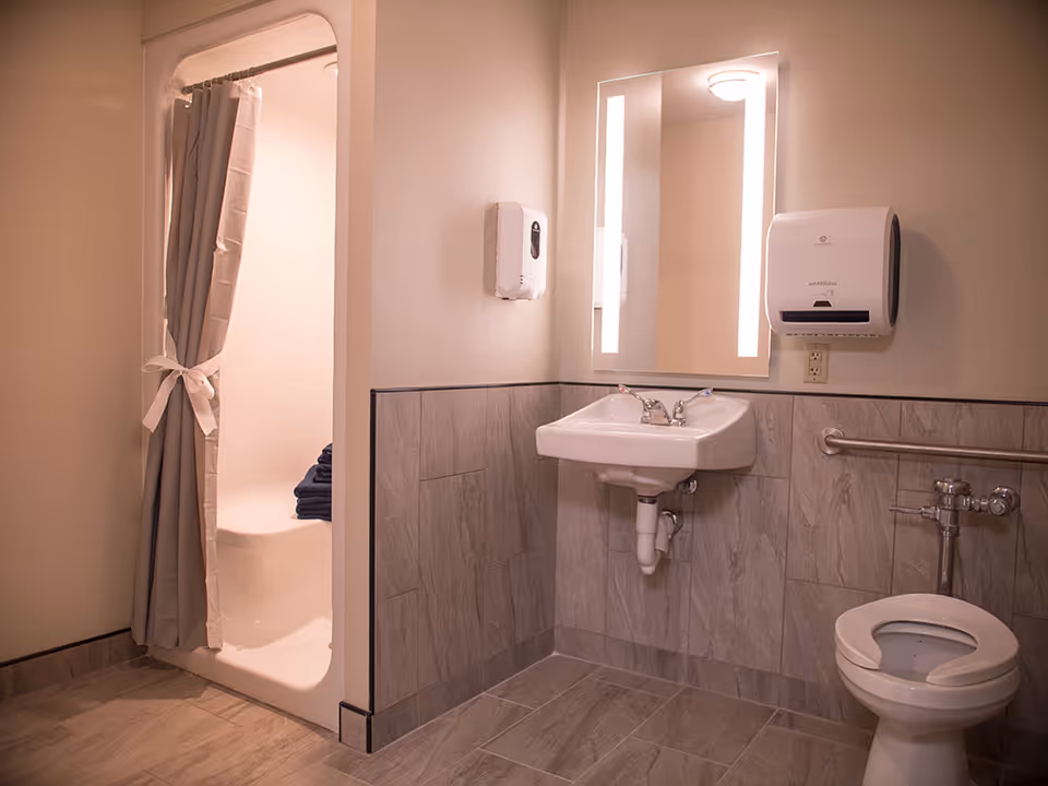 Public bathroom in a senior facility featuring sink, mirror, toilet, and shower.
