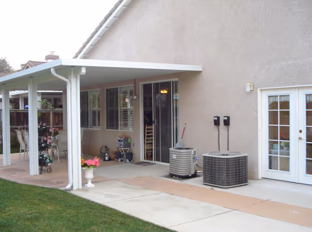 Back patio of a senior living facility with sliding doors, chairs, and air conditioning units.