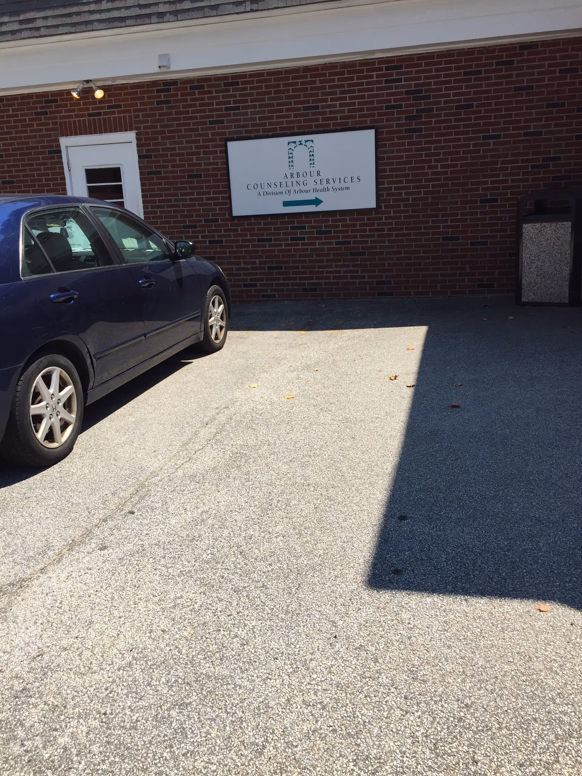 Brick exterior with a parked blue car and Arbour Counseling Services sign.