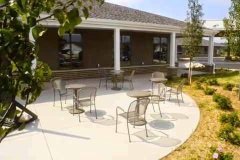 Outdoor curved patio with metal tables and chairs in front of a senior living facility.