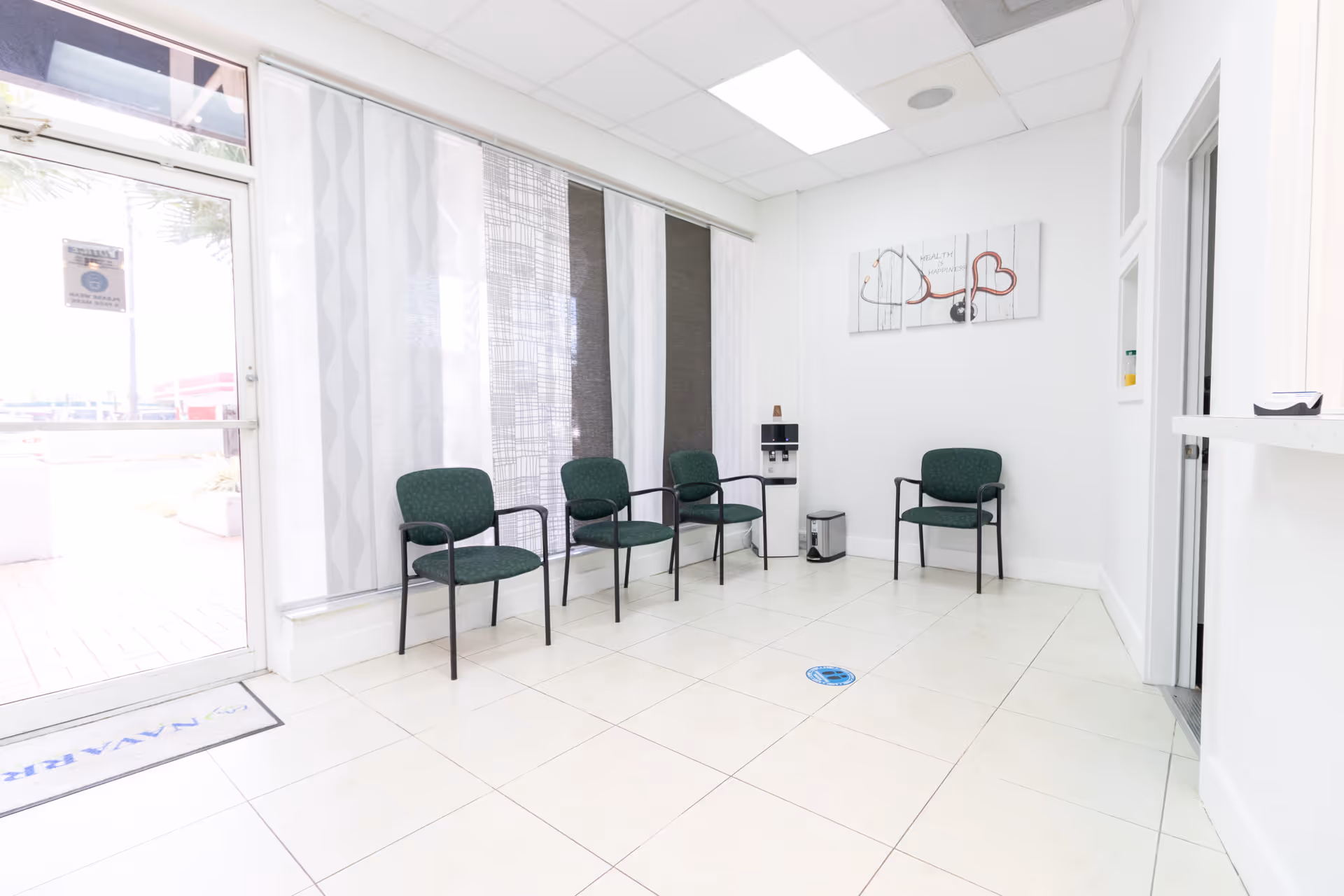 Bright waiting area with several green chairs and a water cooler.