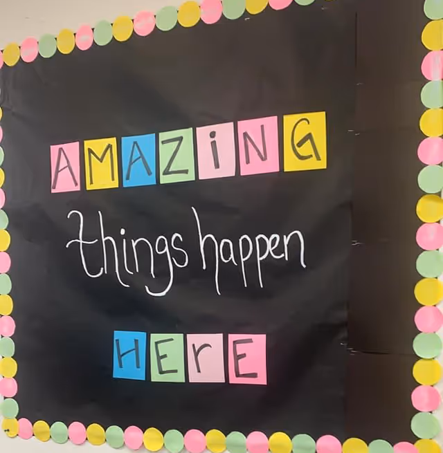 A black wall banner with colorful letters reading Amazing things happen here and a multicolored border.