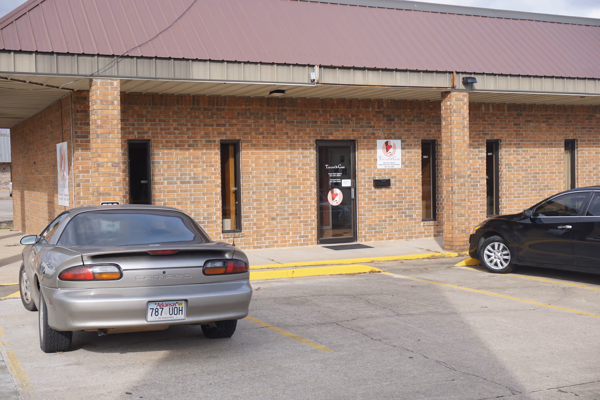 Brick building exterior with a glass entrance labeled Touch of Care and parked cars.