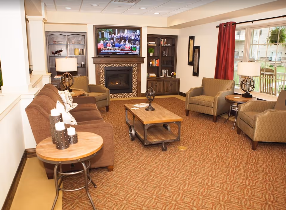 A cozy retirement community living room with a fireplace, wall-mounted TV, sofa and armchairs around a wooden coffee table.