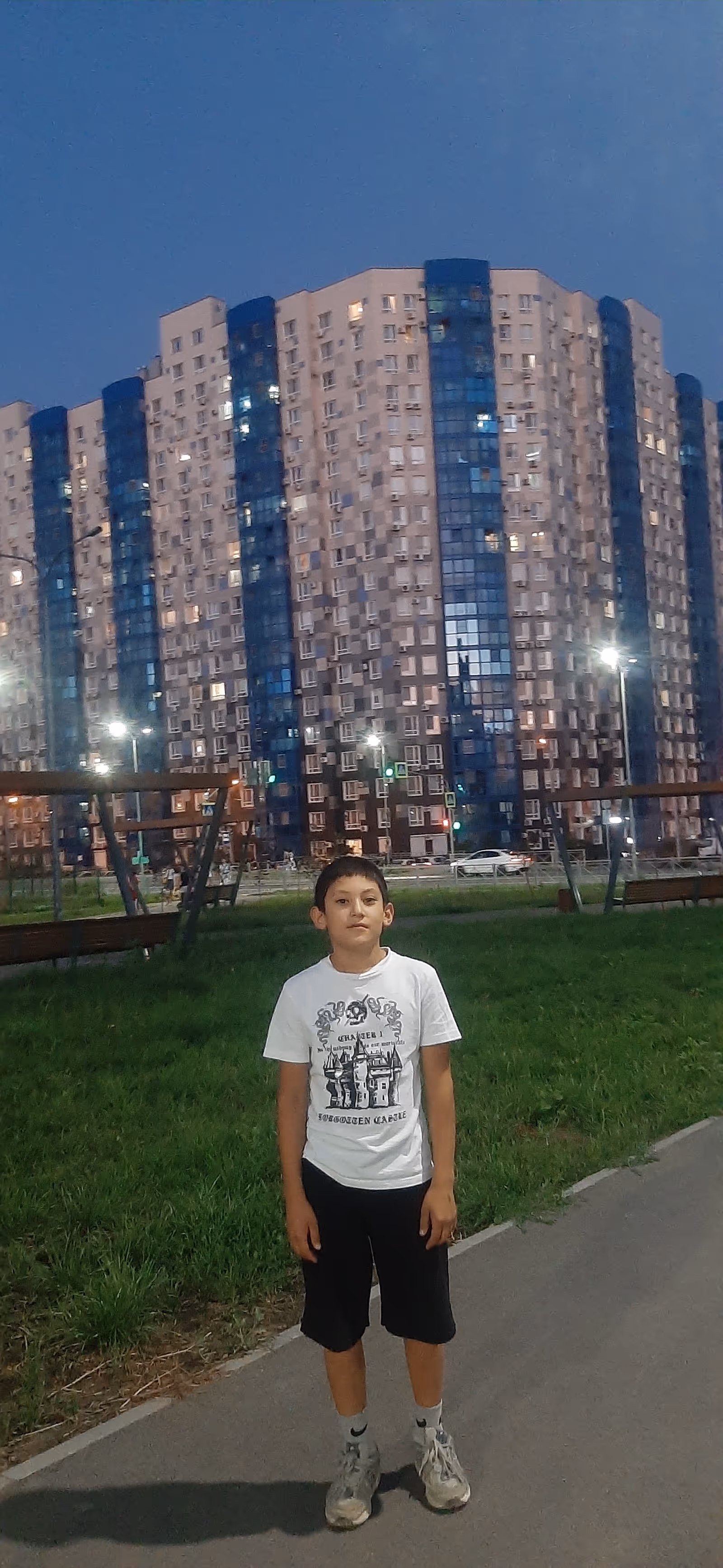 Outdoor park area with a boy in foreground and a tall residential building behind.