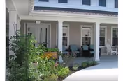 Covered porch with chairs and potted plants in front of a senior living building.