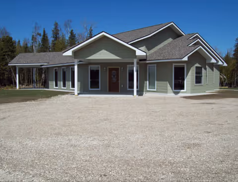 Front exterior view of a green senior living facility with a covered entry and gravel surroundings.