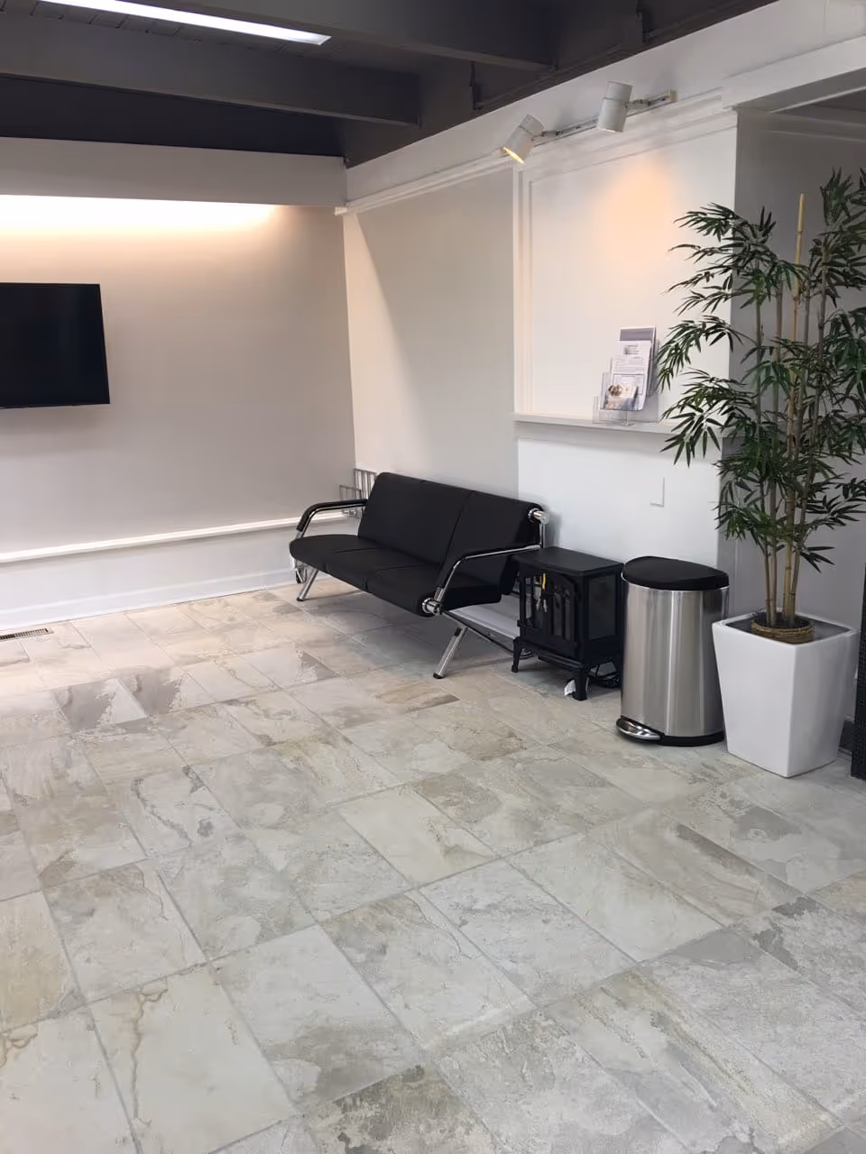 Modern lobby seating area with black couch, TV, plant, and tiled floor.