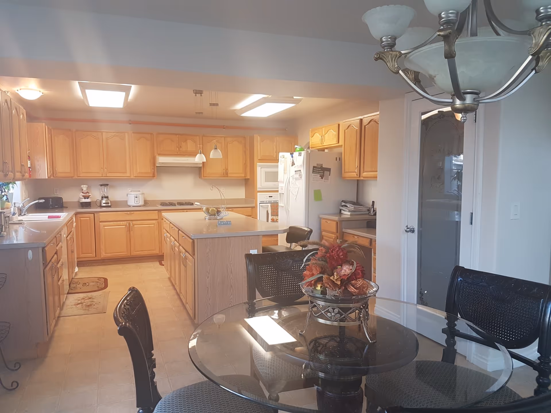 Bright kitchen with wooden cabinets, central island, and glass dining table in foreground.