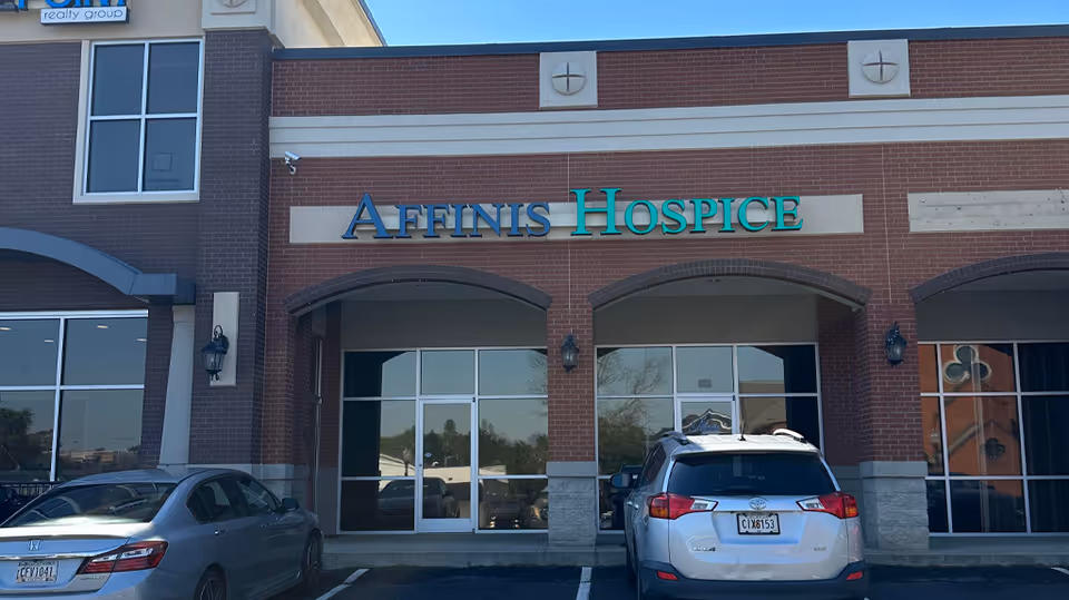 Brick hospice facility with 'AFFINIS HOSPICE' sign and cars parked in front.