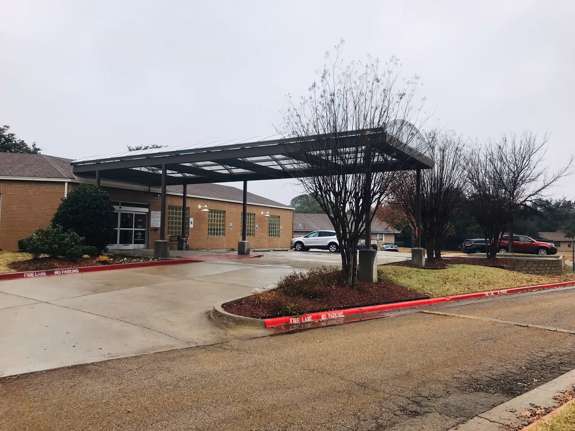 Exterior view of Arlington Villas facility with driveway, canopy, and parking area.