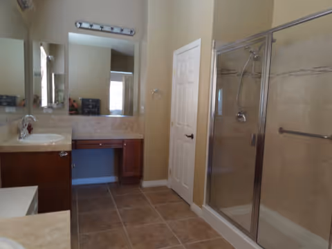 Bright bathroom in a senior living facility with a vanity, mirror, and glass shower.