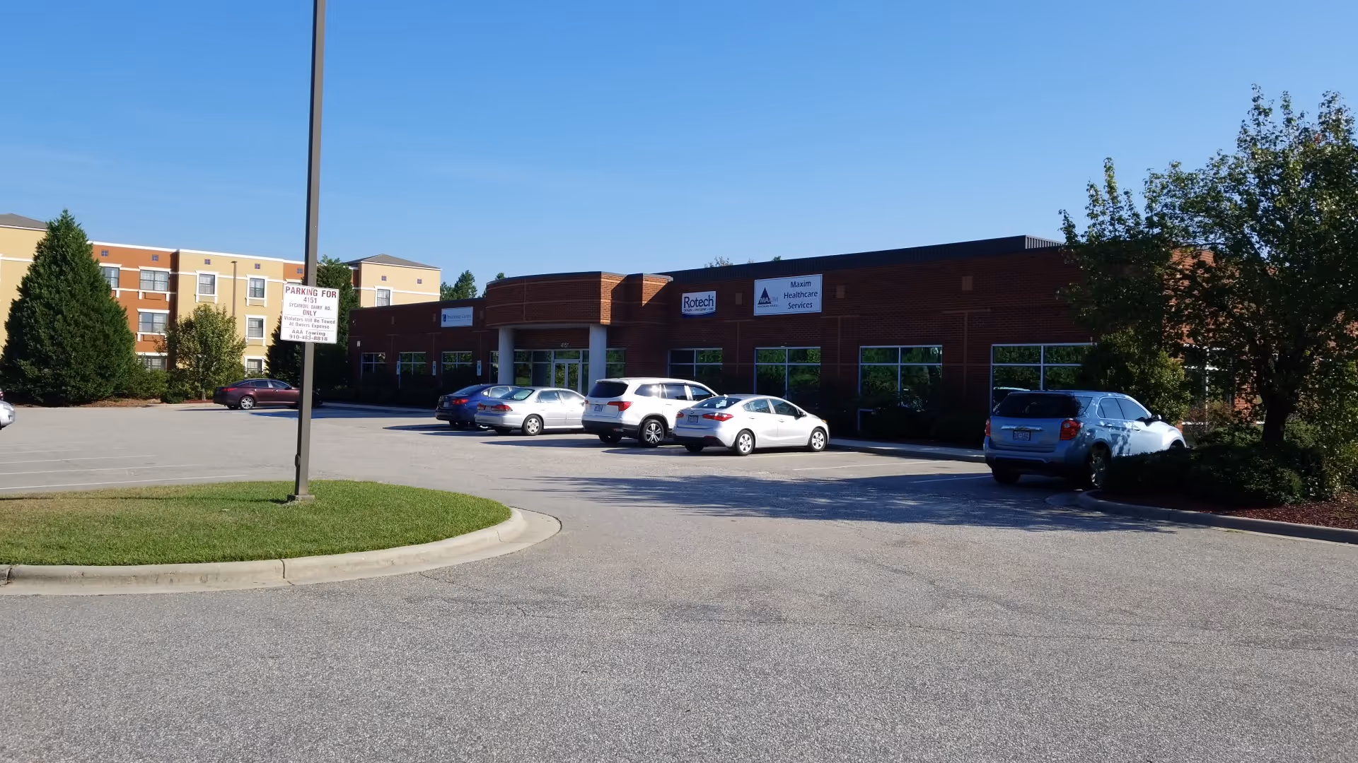 Brick healthcare building with a curved driveway, parking lot, and several cars parked outside.