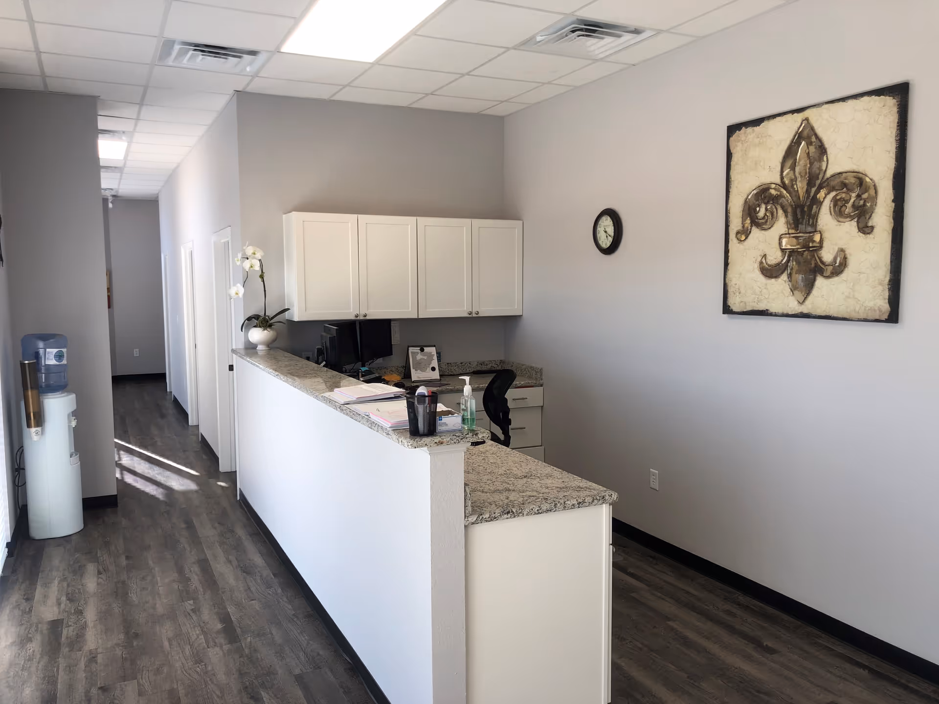 Reception desk along a hallway with granite counter, cabinets, and wall art.