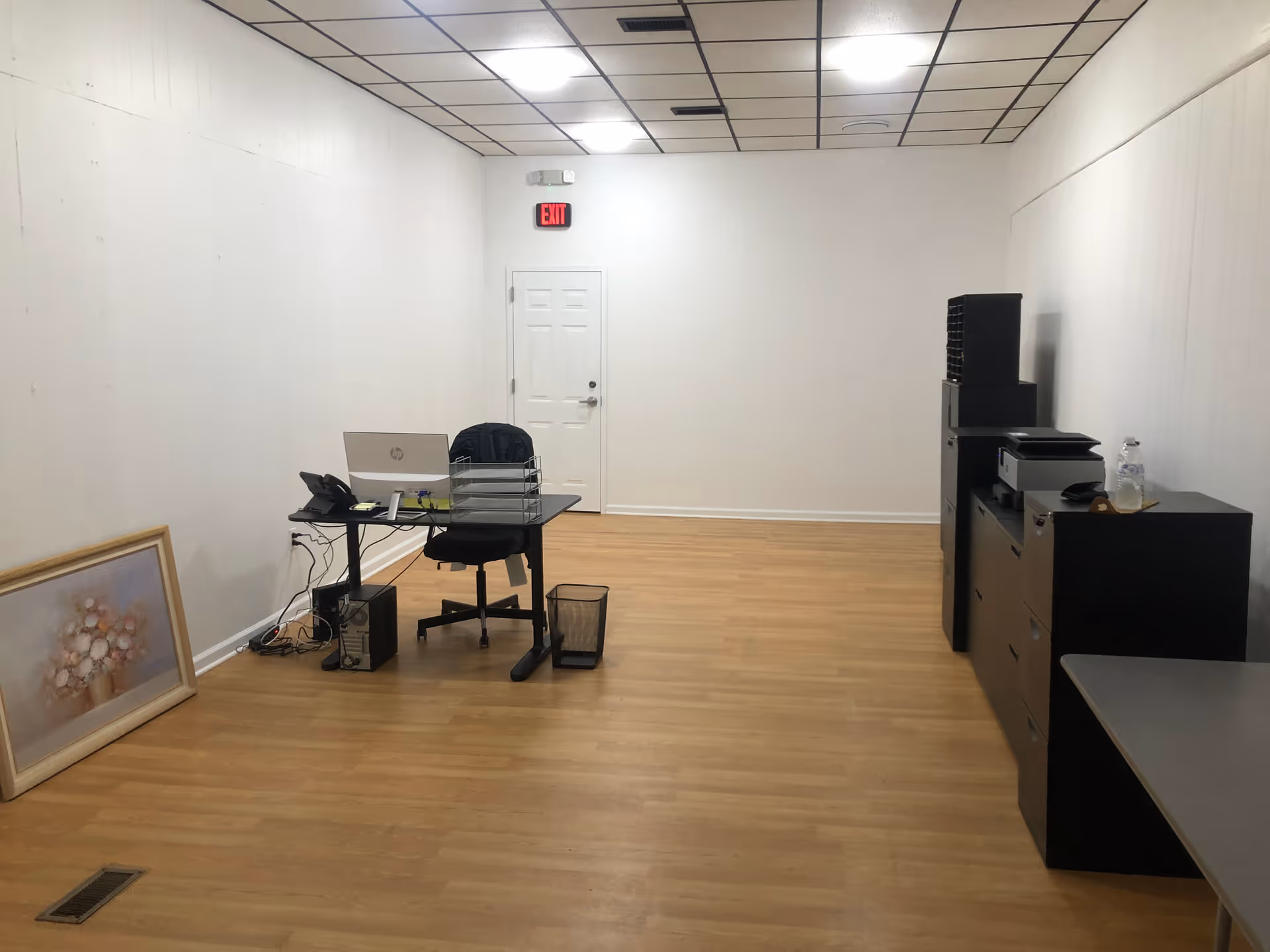 Empty office space with desk, computer, printer, filing cabinet, and painting