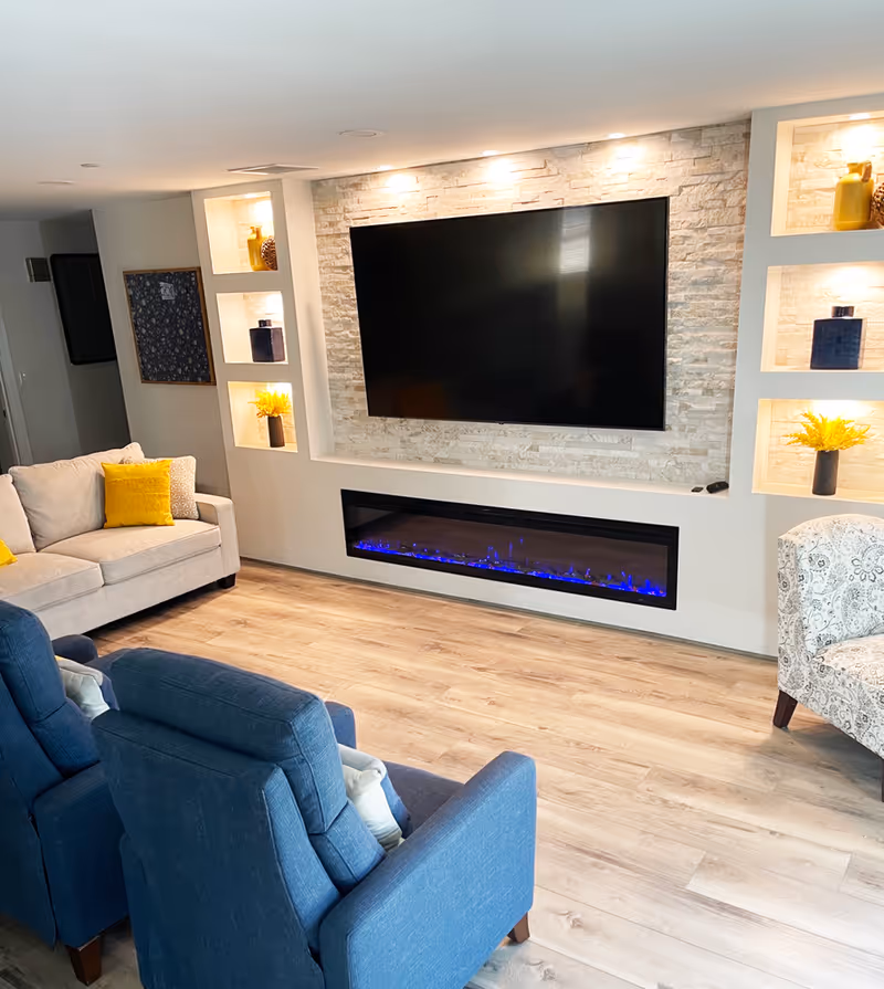 A modern senior living living room featuring a TV, fireplace, and built-in shelves.