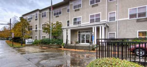 Front exterior of a senior living building with entrance stairs and surrounding greenery.