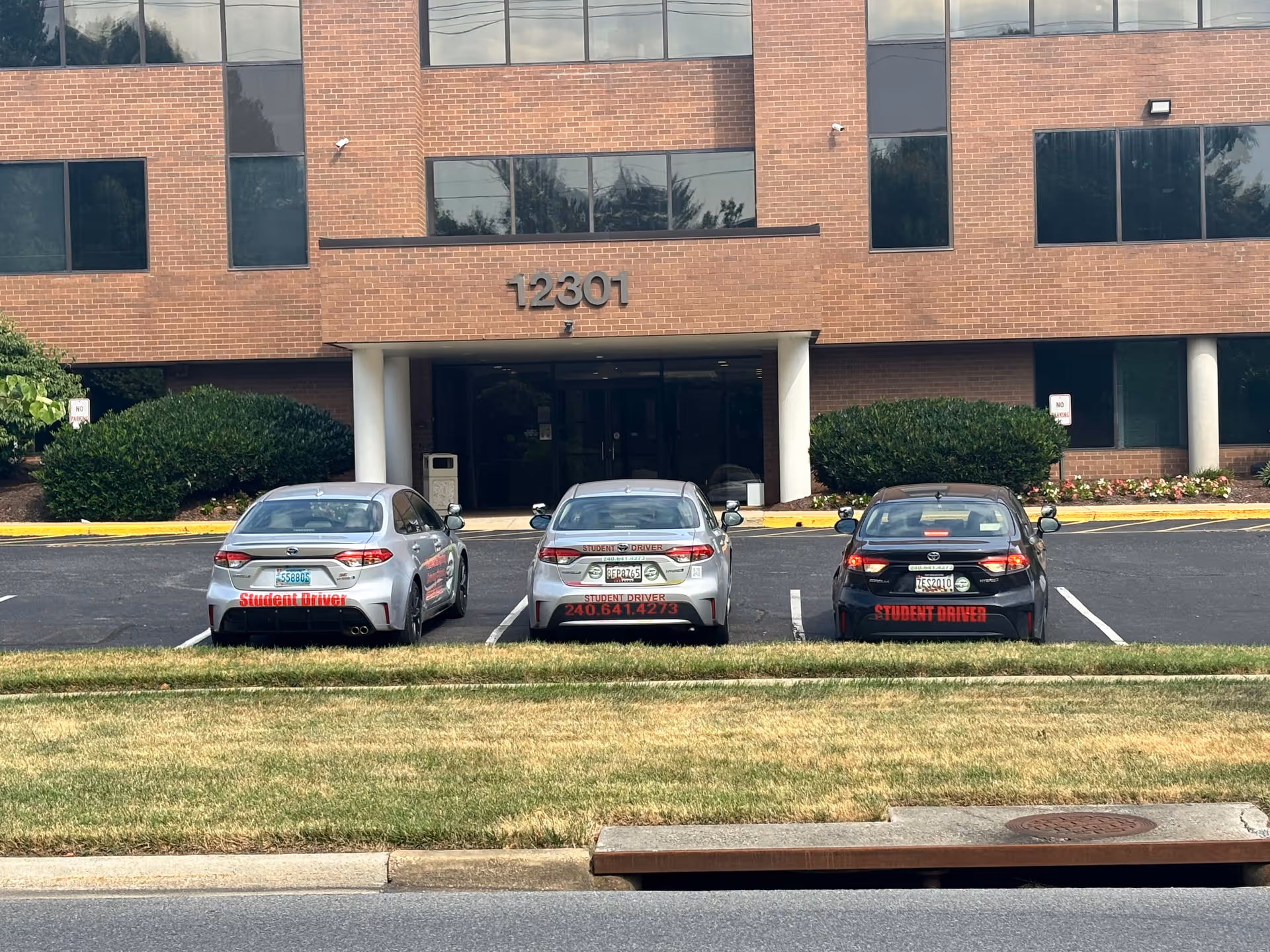Brick building front with three cars parked outside and a glass entrance.