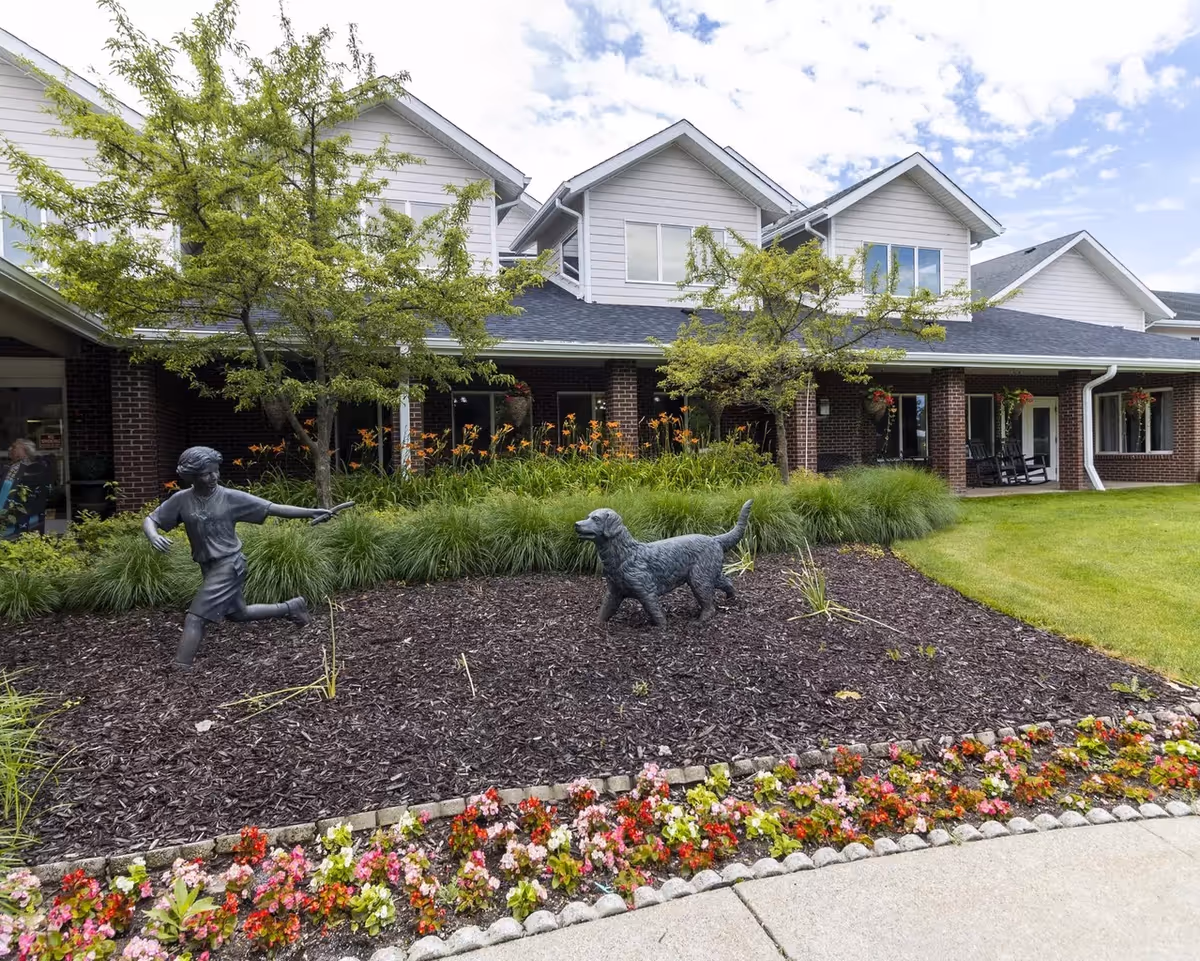 Exterior view of StoryPoint Grand Rapids West with brick building, landscaping, and statues.