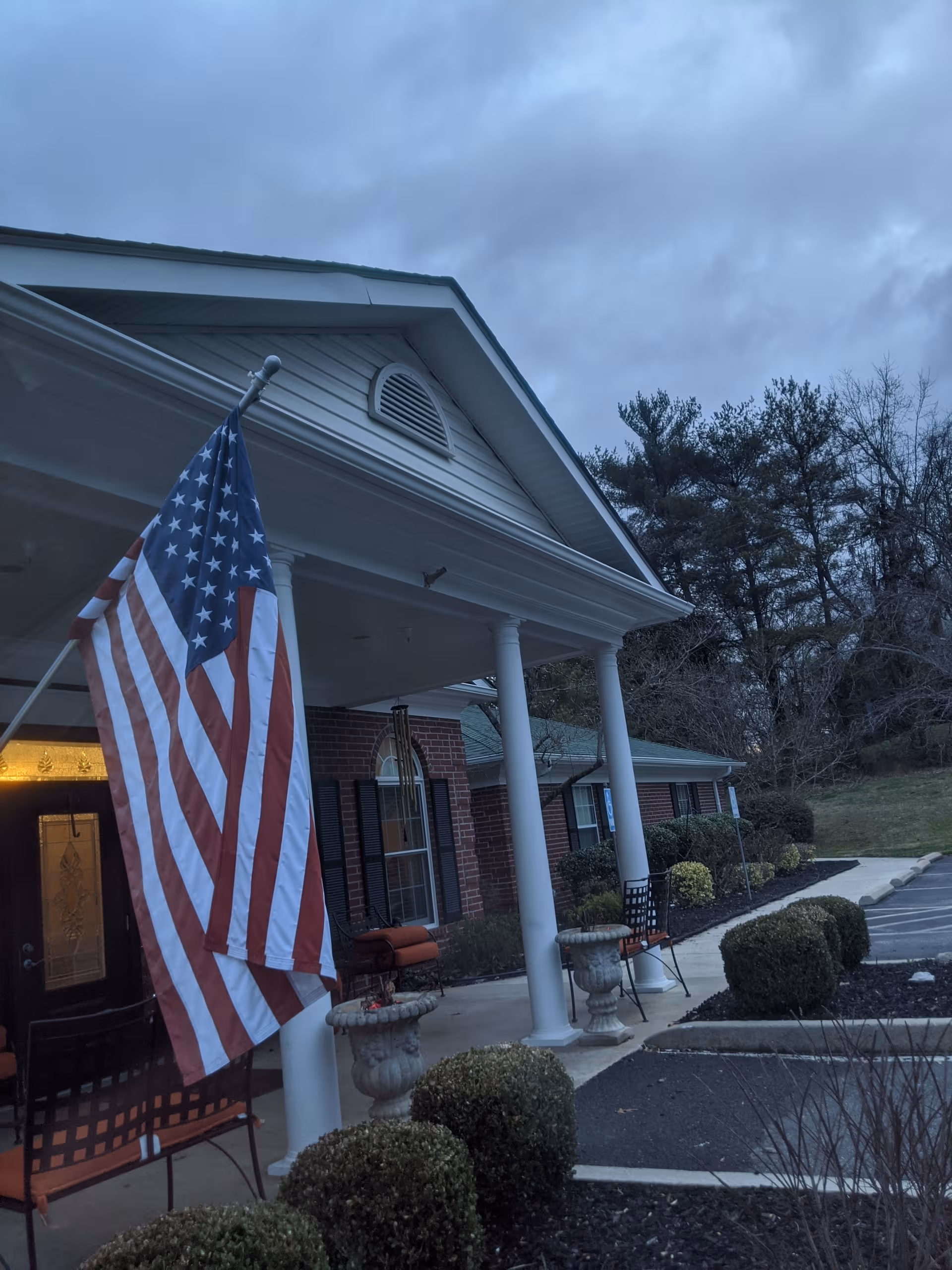 Front exterior of Riverview Terrace with flag, columns, and seating on the porch.