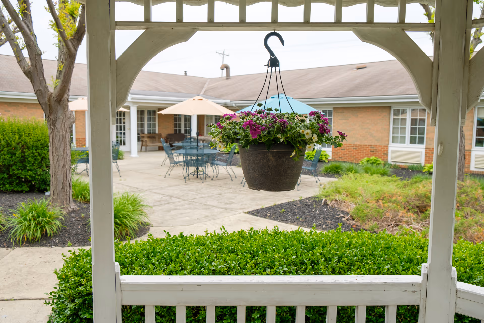 Hanging flower basket under a white gazebo overlooks an outdoor seating courtyard.
