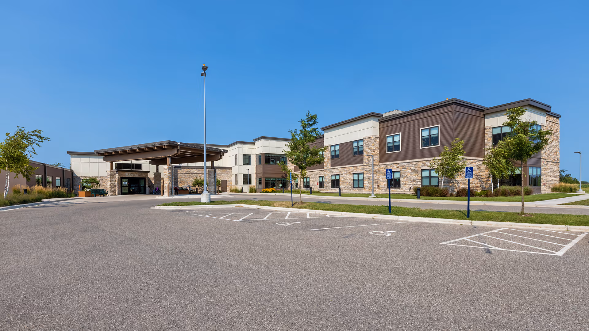 Front exterior of a modern senior living facility with a parking lot and entrance canopy.
