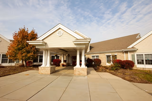 Senior living facility exterior with a covered entrance, columns, and landscaped walkway.