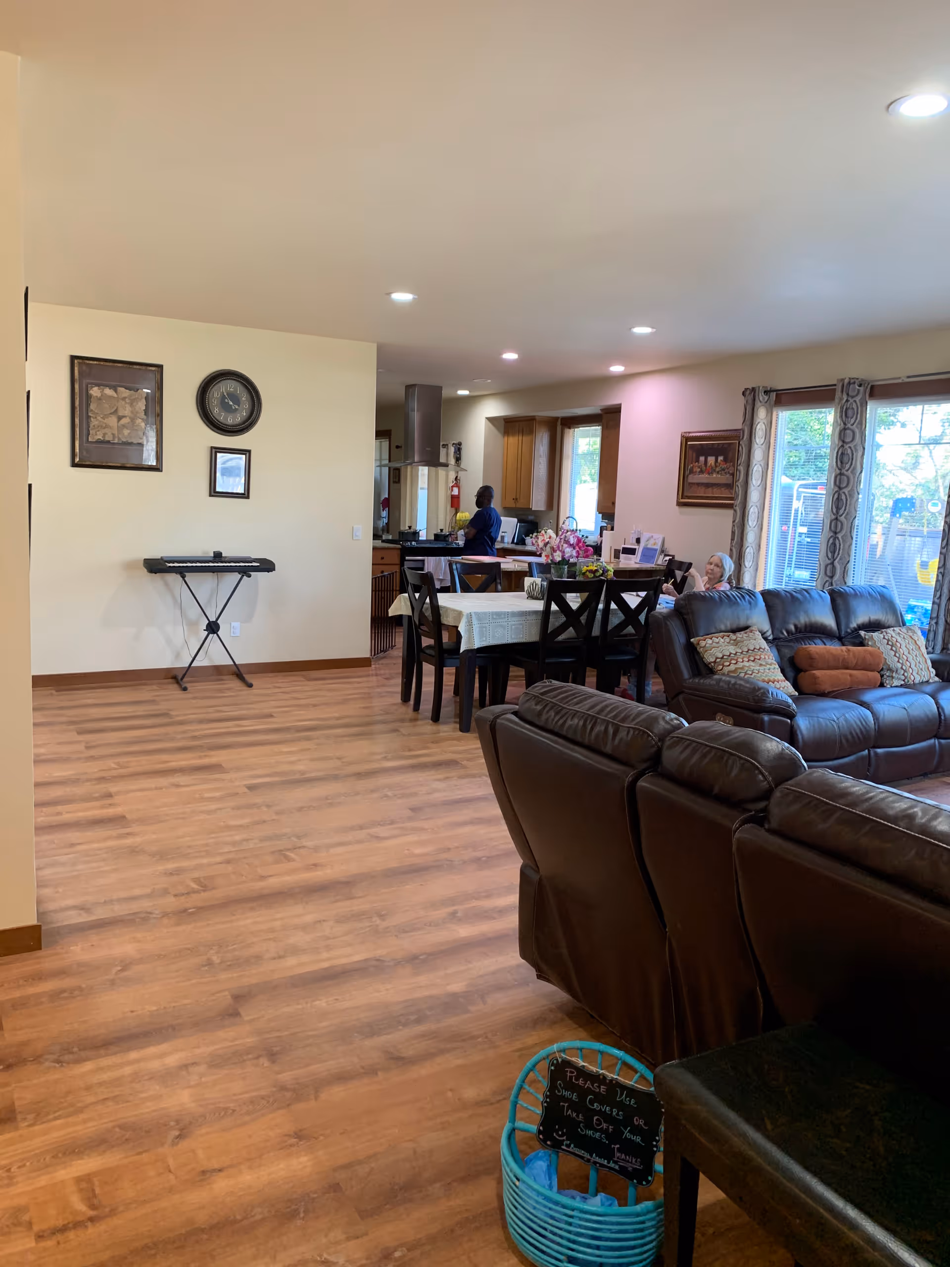 Open senior-living living-dining space with brown leather sofas, dining table, and kitchen in the background.