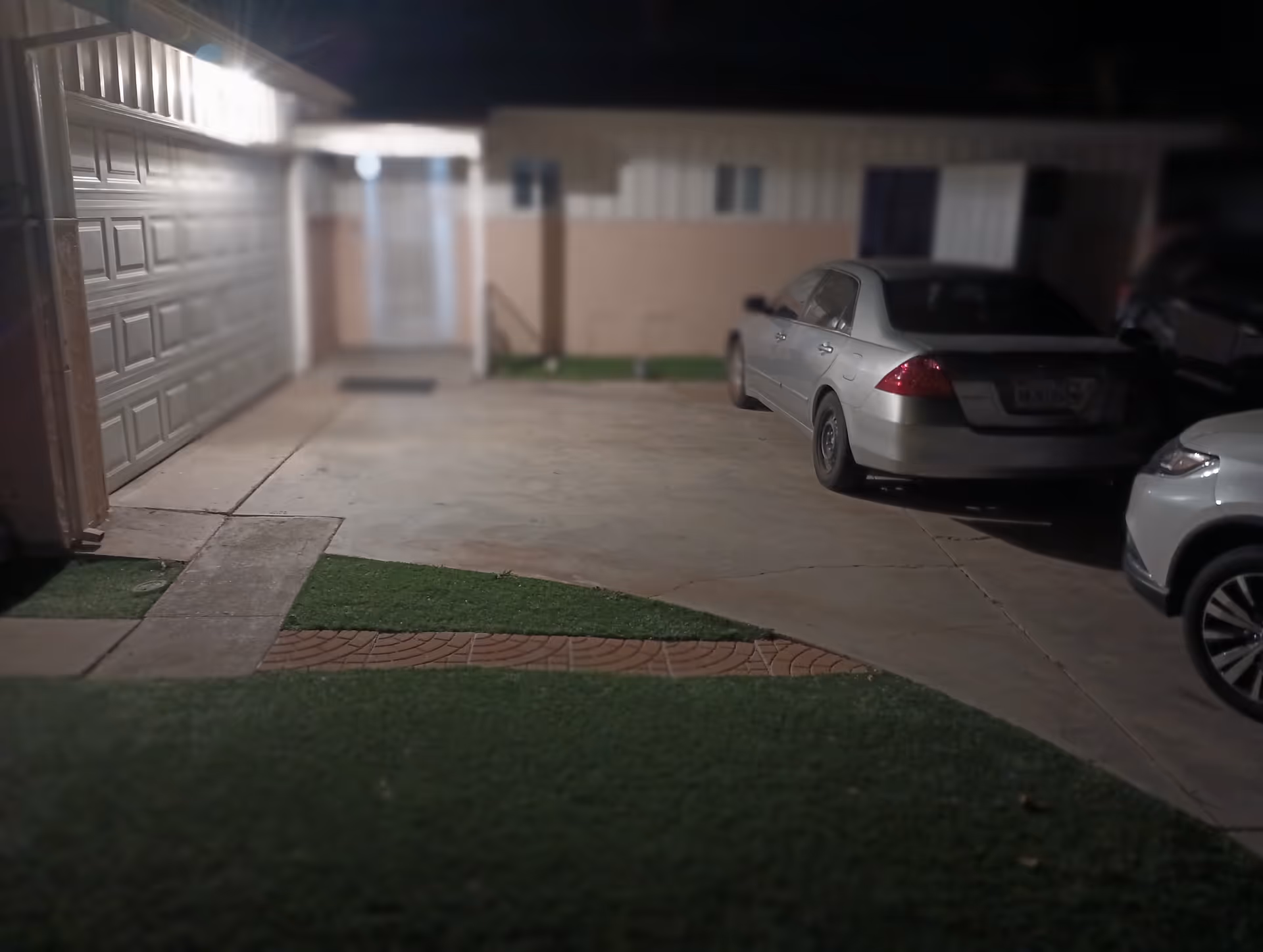 Night exterior of a building with a driveway, garage doors, and parked cars.