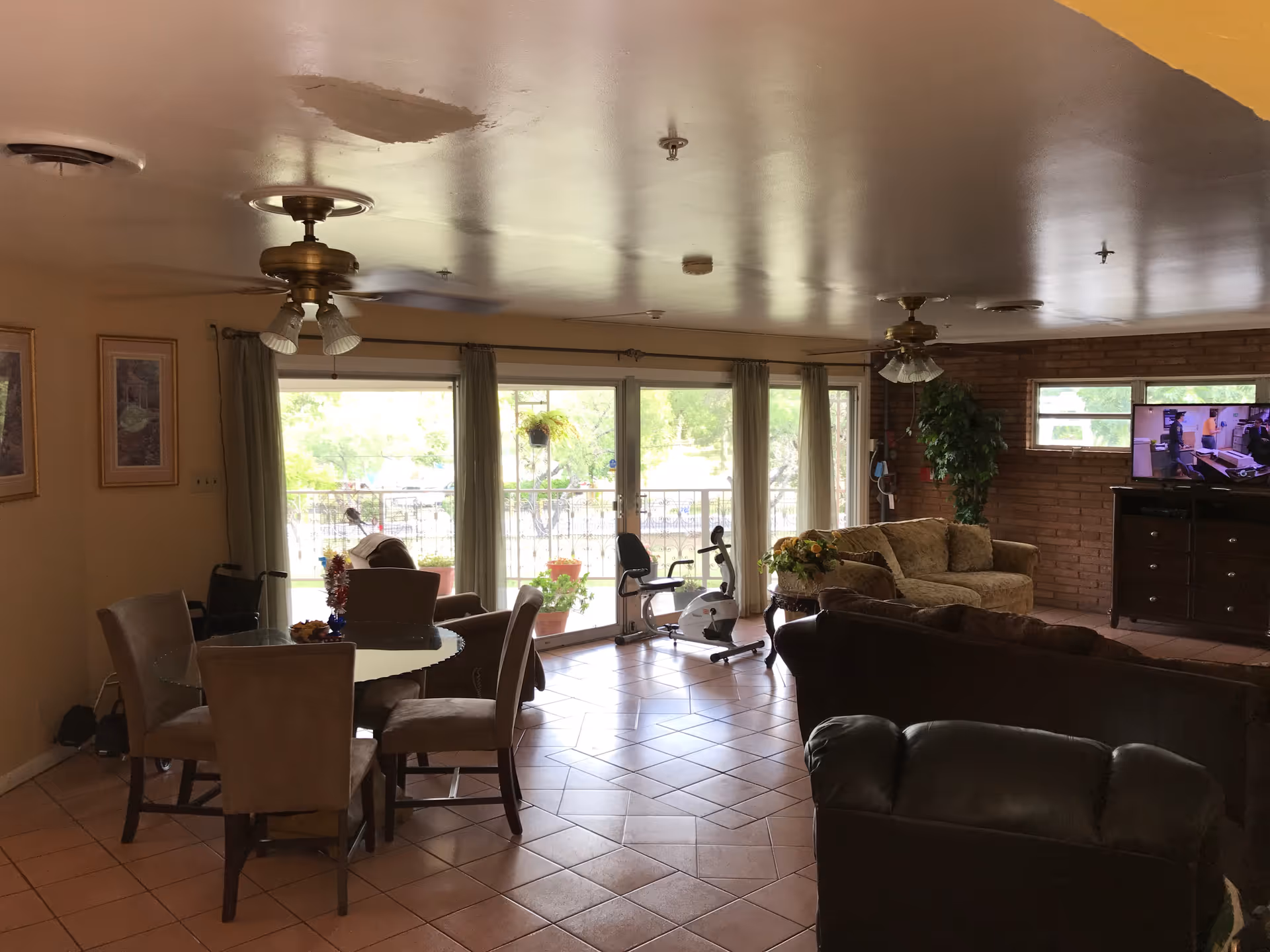 Spacious living area with dining set, sofas, exercise bike, brick accent wall, and sliding doors.