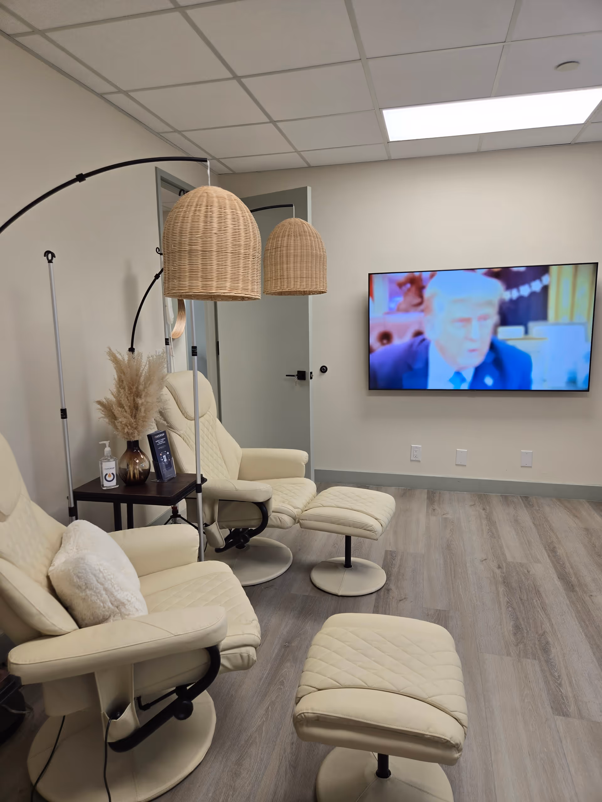 Cream recliners and ottomans in a senior living lounge with wicker lamps and a wall TV.