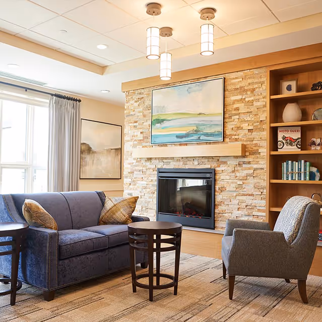 Cozy living room with blue sofa, armchair, fireplace, stone wall, and built-in shelving.