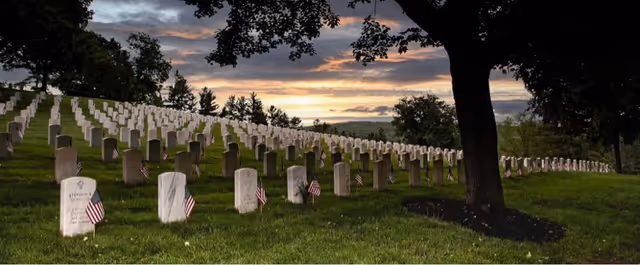 Rows of white gravestones with small American flags in a cemetery at dusk