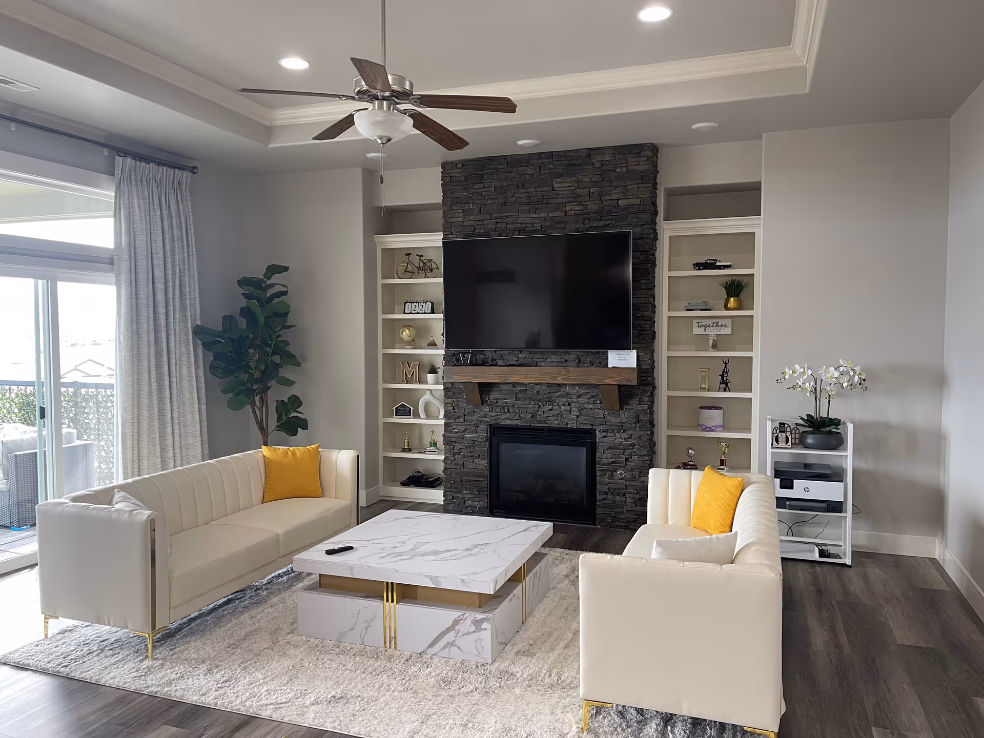Modern living room with white sofas, a stone fireplace, and built-in shelves.