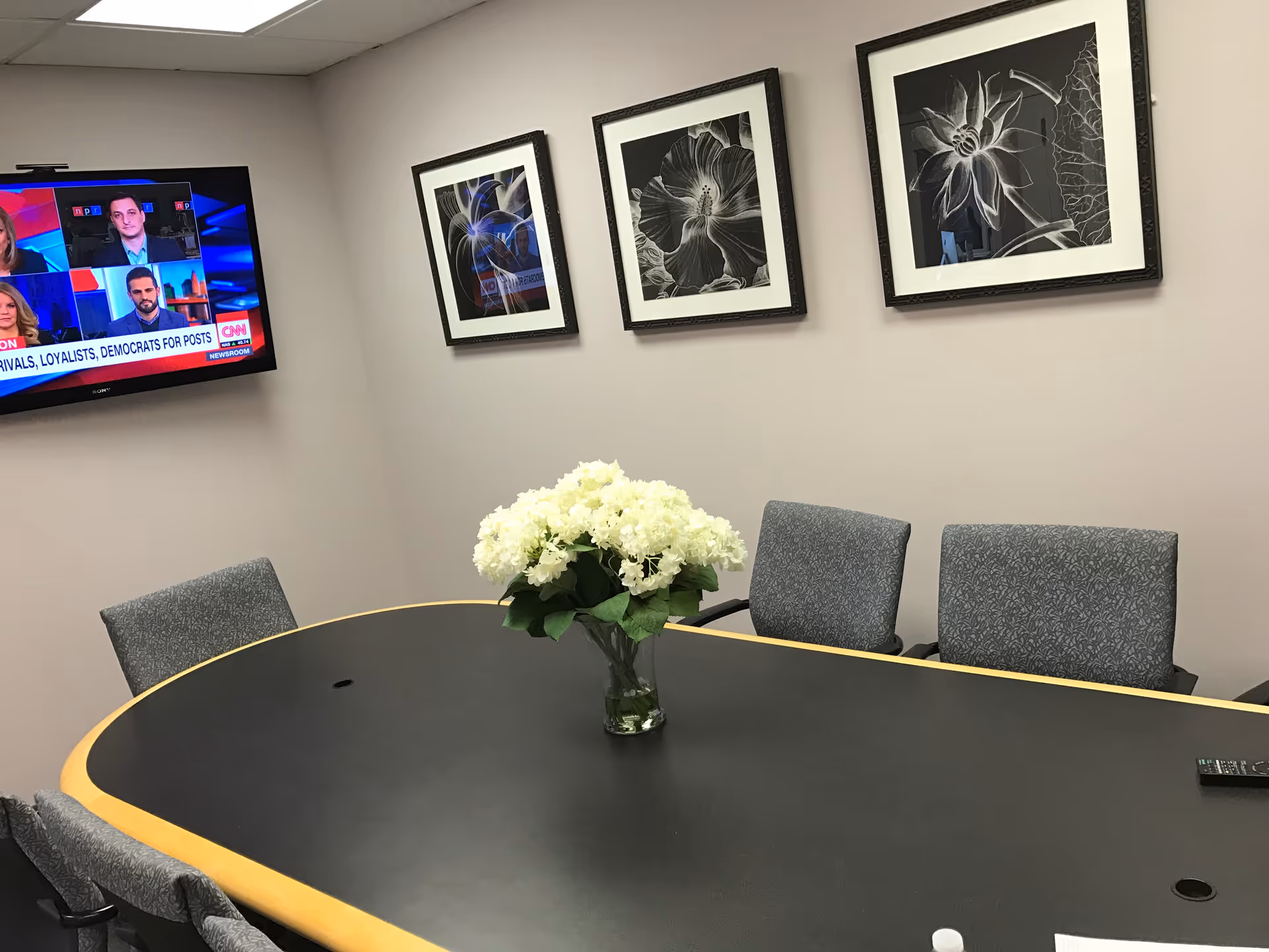 Conference room with oval table, flower centerpiece, wall art, and a TV.