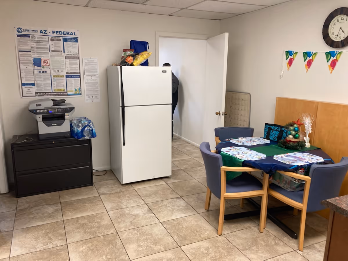 Indoor dining area with a round table, chairs, fridge, and copier.