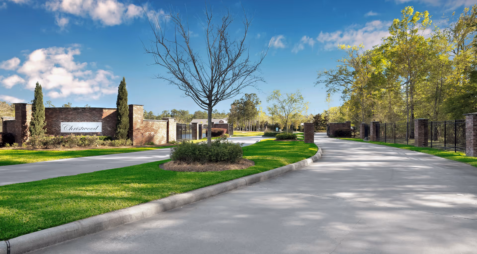 Driveway entrance to Christwood Retirement Community with brick signage, gated fences, landscaped median and trees.