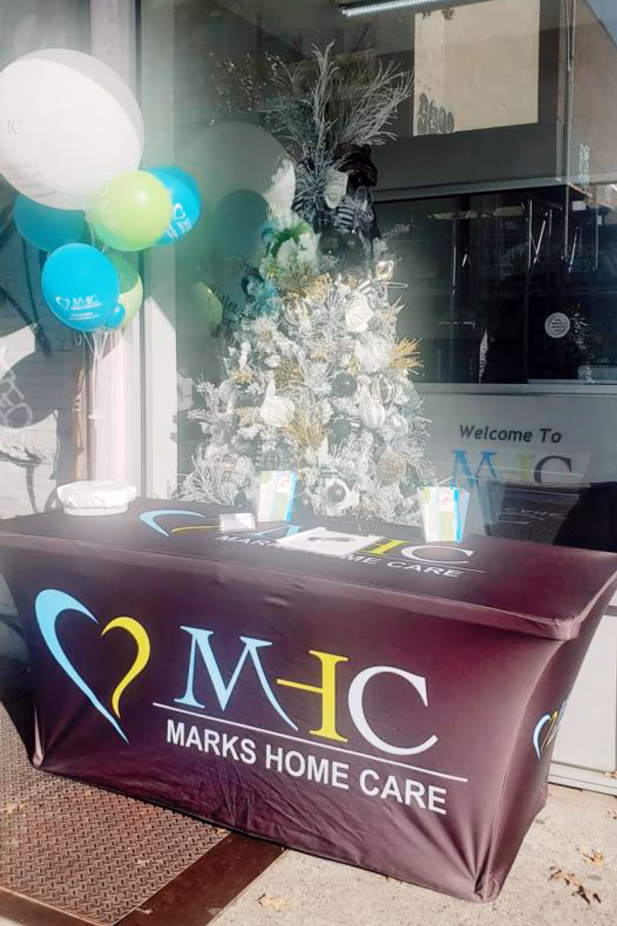 Promotional table with Marks Home Care branding, balloons, and decorations at the entrance.