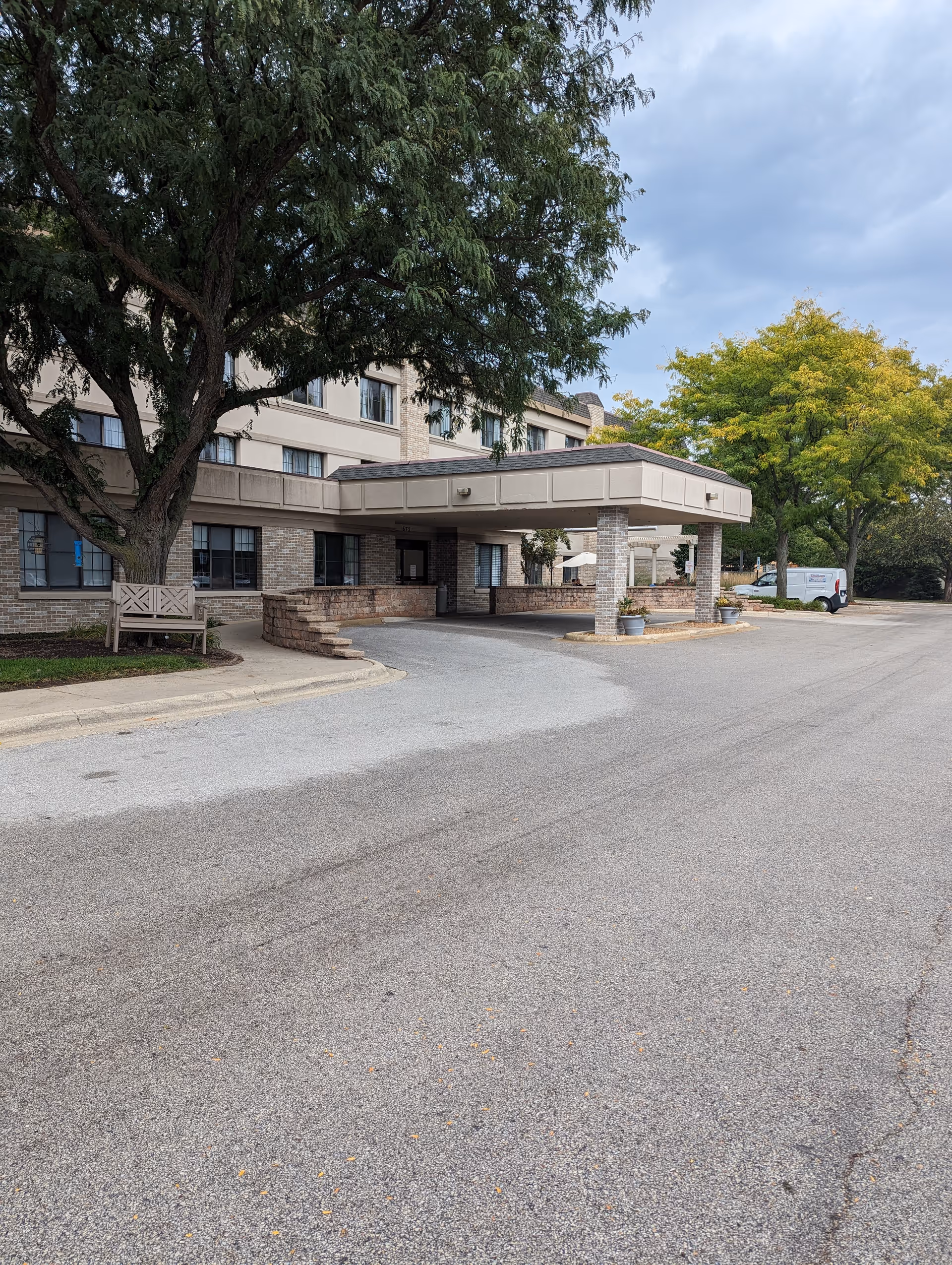 Senior living facility entrance with covered drop-off area and surrounding trees.