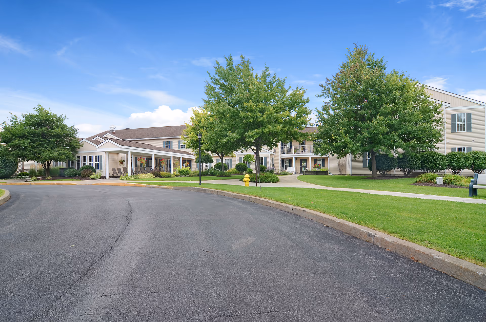 Wide exterior view of Brookdale Summerfield with trees, grass, and curved entrance road.