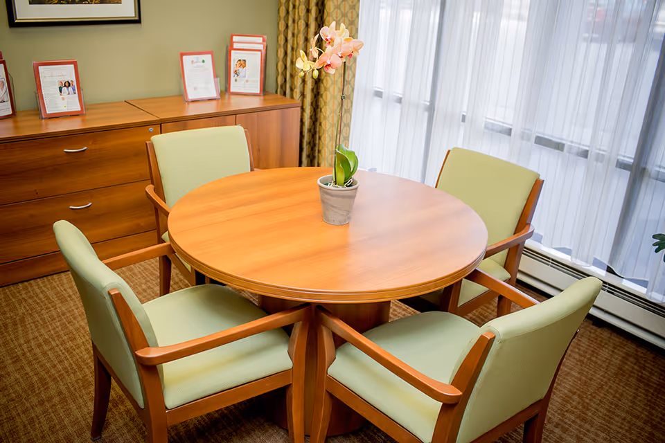 Round wooden table with green chairs in a senior facility dining room.