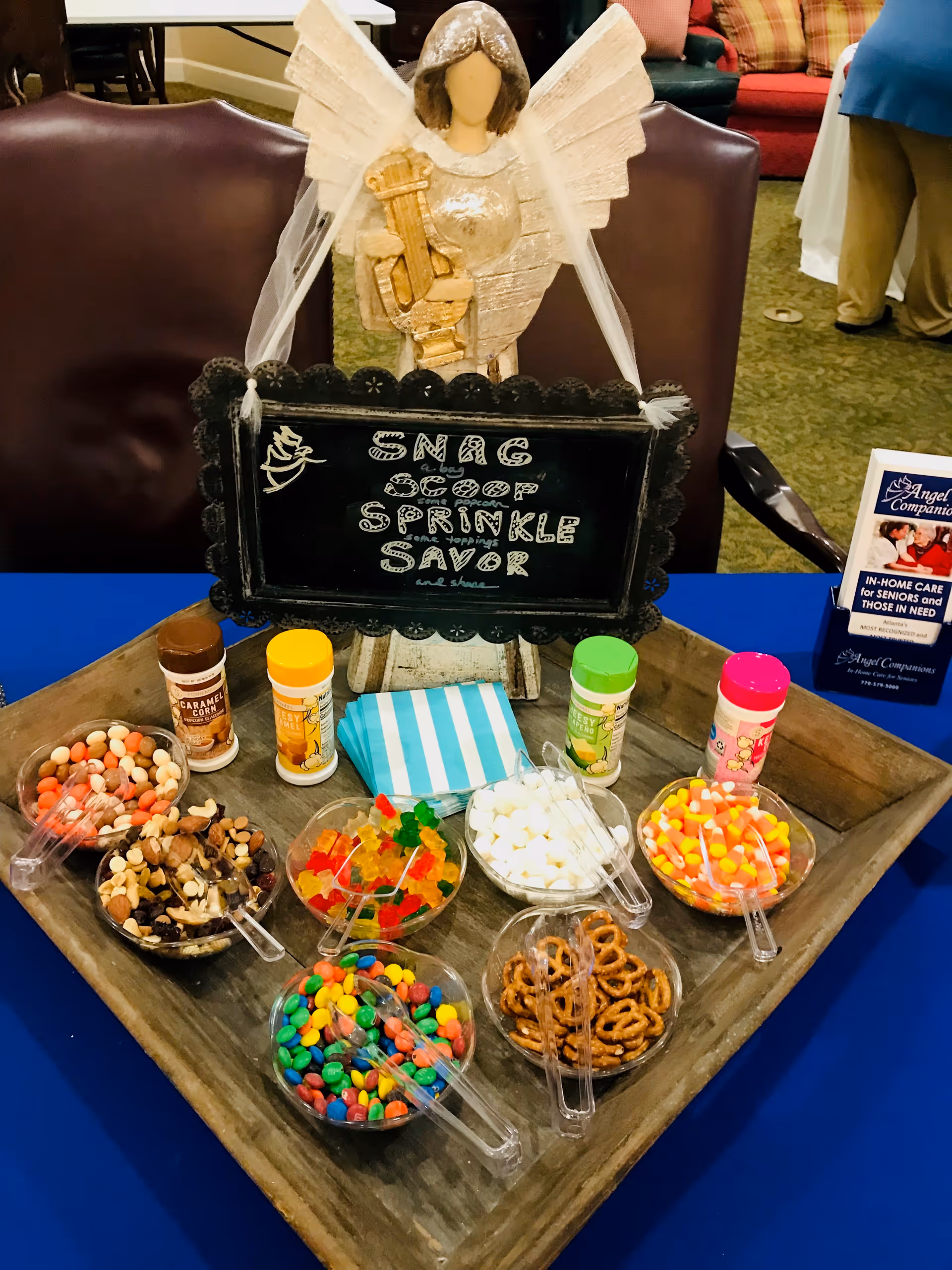 Assorted candies and snacks displayed on a wooden tray with an angel statue centerpiece.